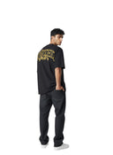 Hombre vistiendo camiseta negra de algodón Corteiz Royale con logo amarillo en la espalda de One Kickz