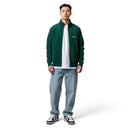 Hombre vistiendo chaqueta One Kickz Corteiz de punto acanalado verde con cremallera sobre camiseta blanca y jeans
