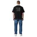 Vista trasera de un hombre con polo negro Corteiz Alpine con el numero 18 bordado y parches decorativos