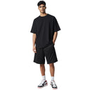 Modelo vistiendo pantalones cortos negros Corteiz Dem Pro de One Kickz con camiseta negra y zapatillas deportivas