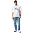 Modelo vistiendo camiseta blanca Corteiz Kingdom Tee de One Kickz con estampado gráfico negro y jeans azules