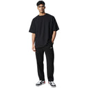 Modelo vistiendo pantalones de chándal Corteiz Pista de terciopelo negro de One Kickz con camiseta negra y zapatillas