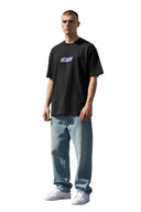 Modelo vistiendo camiseta negra Corteiz Snickers con logo gráfico en el pecho, estilo urbano